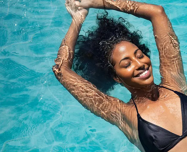 Mulher sorrindo de olhos fechados enquanto flutua relaxada em uma piscina