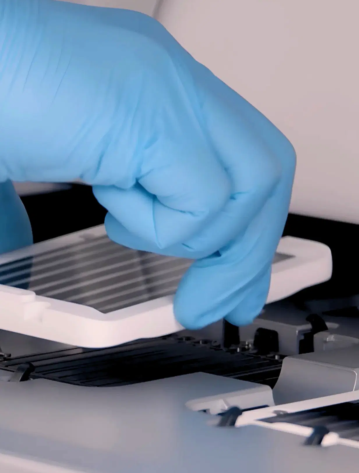 Mão com luva azul posicionando lâmina de DNA em equipamento laboratorial de alta precisão